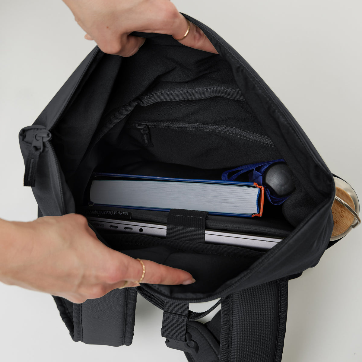 ROLLTOP EASY SMALL Rucksack von einer Frau offen gehalten, um den Innenraum mit Laptop und Buch zu zeigen.