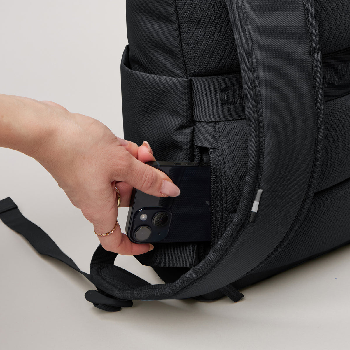 ROLLTOP EASY SMALL Monochrome Edition Rucksack, eine Frau steckt ein Smartphone in die Geheimtasche.