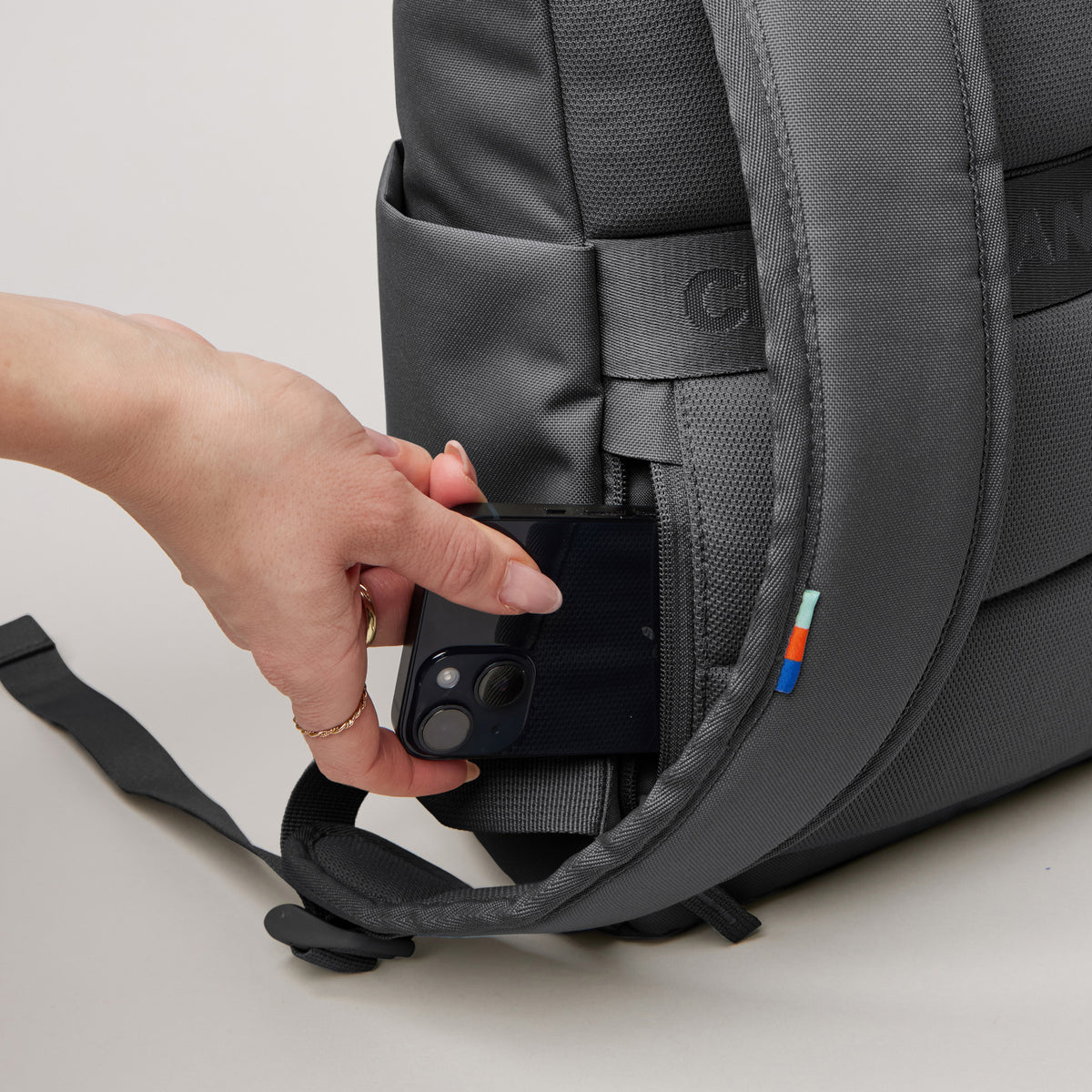 ROLLTOP EASY SMALL Monochrome Edition Rucksack in shark (Dunkelgrau) Hand steckt Smartphone in die Seitentasche.