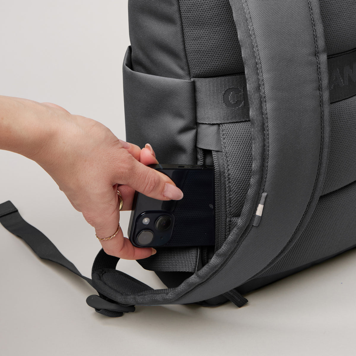 ROLLTOP EASY SMALL Rucksack in shark (Dunkelgrau). Eine Hand steckt ein Smartphone in eine geheime Seitentasche.