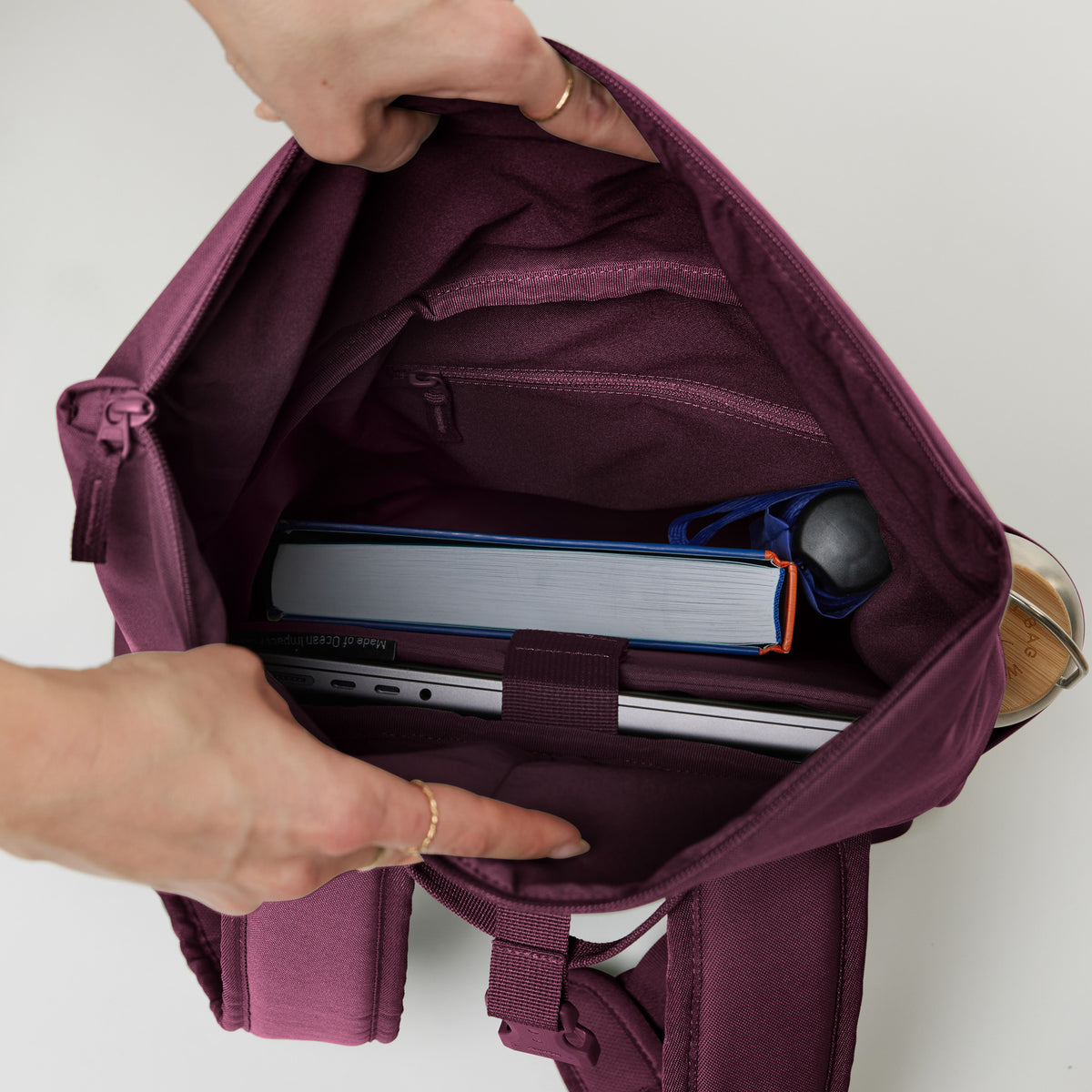 ROLLTOP EASY SMALL Rucksack in kraken (Weinrot), innen von Händen geöffnet, mit Laptop und Buch.