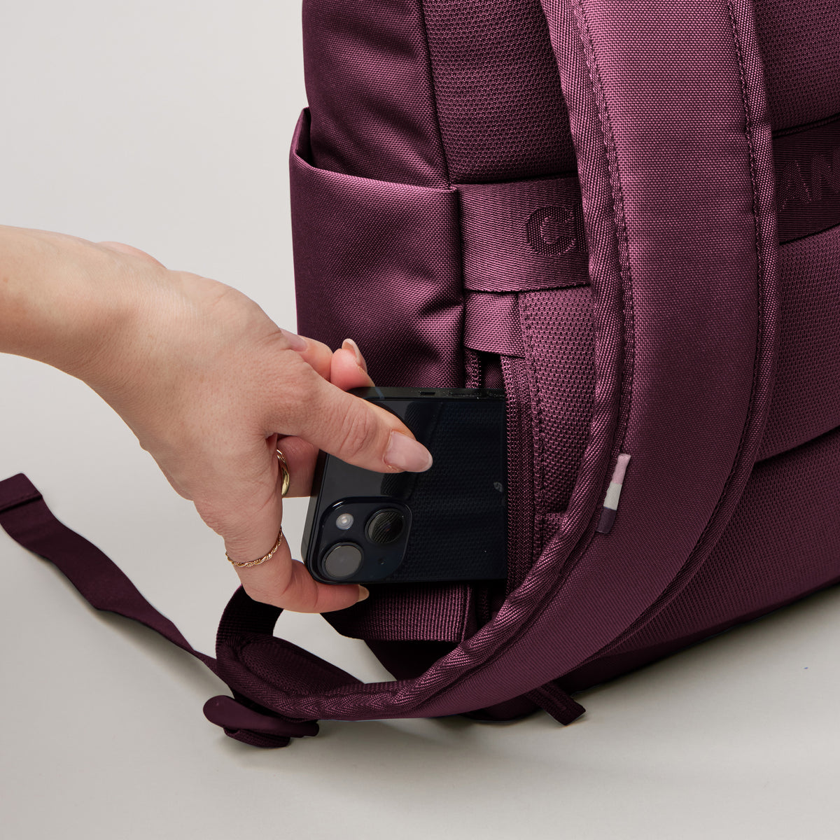ROLLTOP EASY SMALL Monochrome Edition Rucksack in kraken (Weinrot) von einer Frau, die ein Smartphone in eine Geheimtasche steckt.
