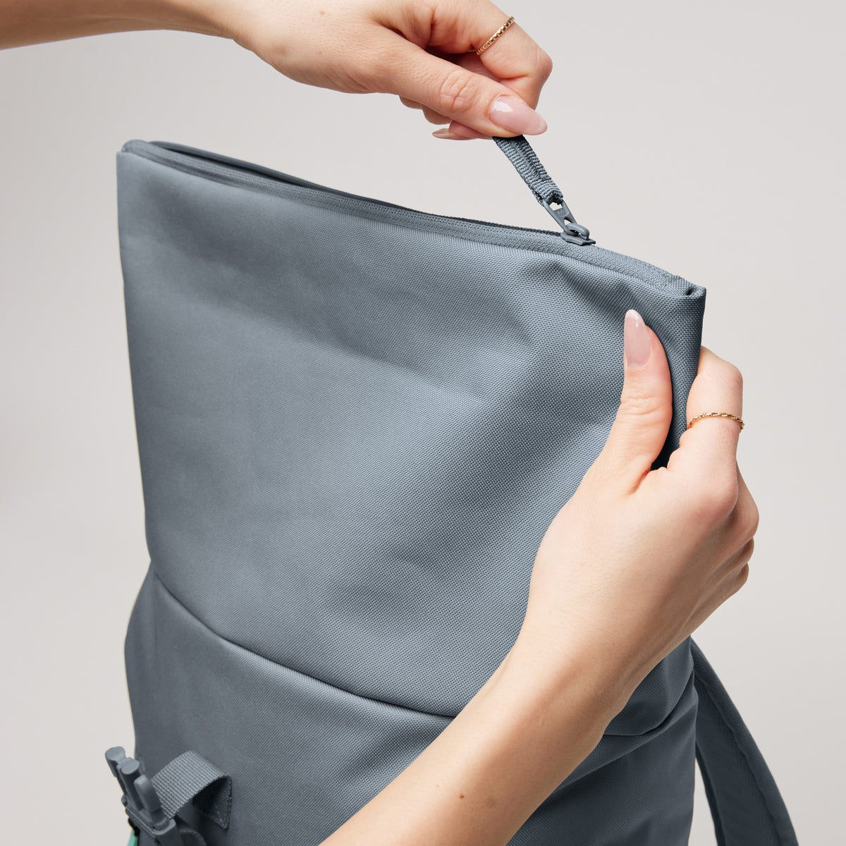 ROLLTOP EASY SMALL Rucksack in marlin (grau-blau), dessen Reißverschluss von Händen bedient wird.