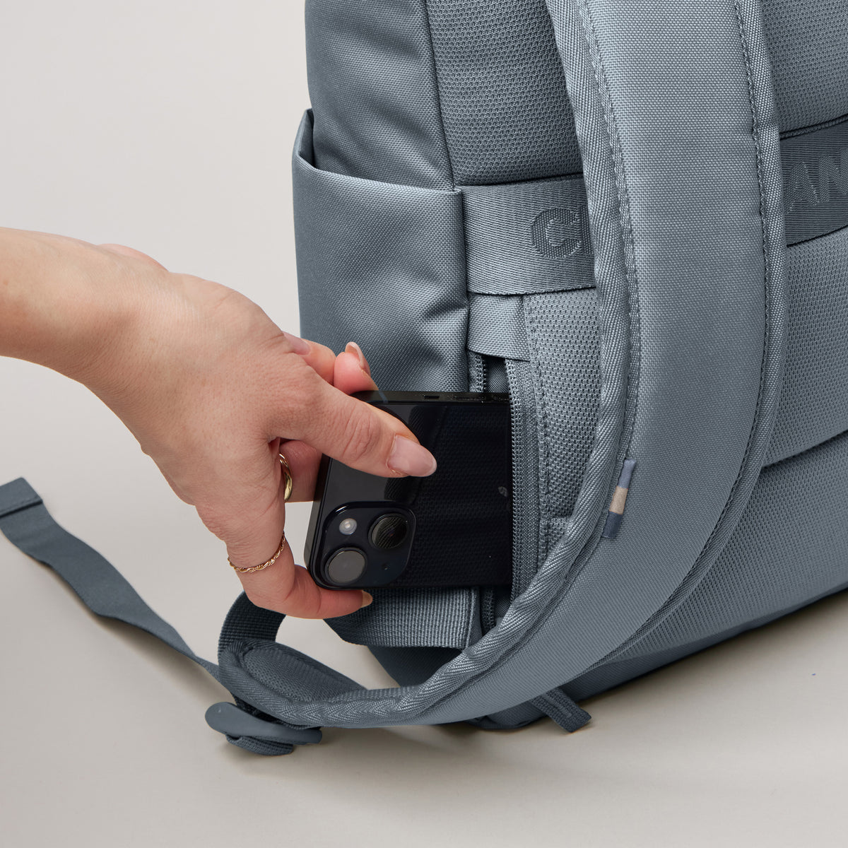 ROLLTOP EASY SMALL Rucksack in marlin (grau-blau), eine Hand steckt ein Handy in eine geheime Tasche.