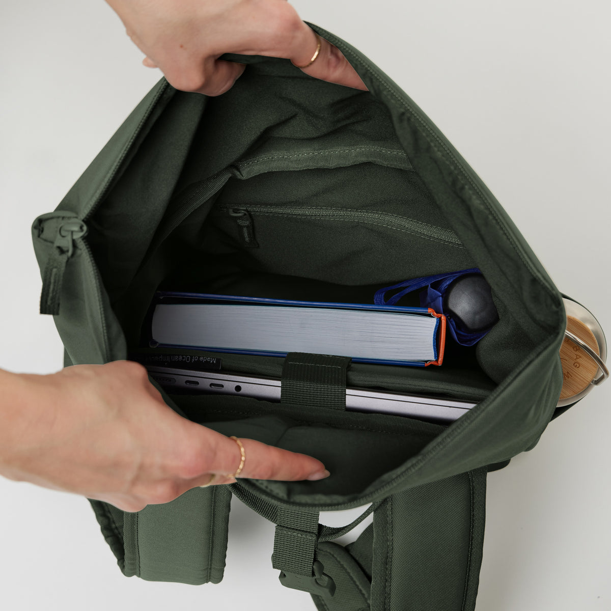 ROLLTOP EASY SMALL Rucksack in algae (Dunkelgrün mit Graustich) mit geöffnetem Innenfach, Laptop und Buch.