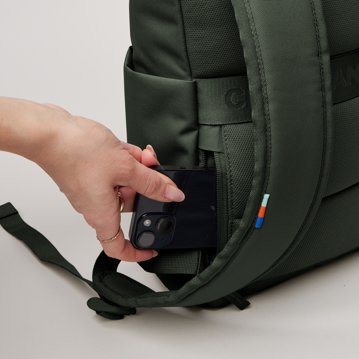 ROLLTOP EASY SMALL Rucksack in algae (Dunkelgrün mit Graustich). Frau steckt Handy in versteckte Seitentasche.