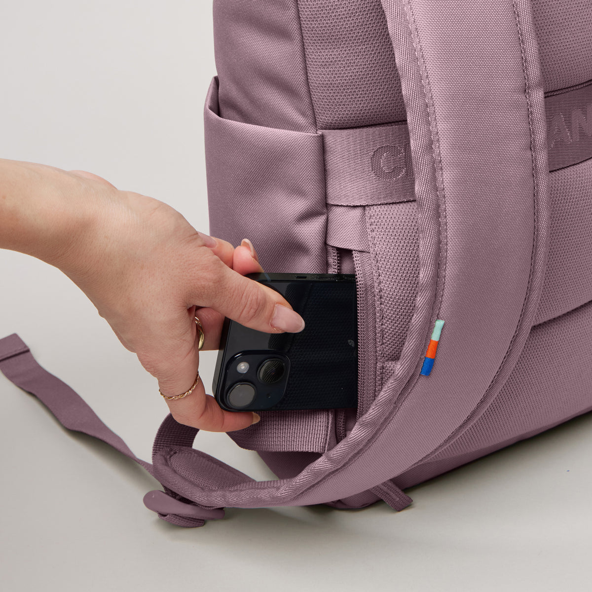 ROLLTOP EASY SMALL Rucksack in calamary (Altrosa), eine Frau steckt ein Handy in eine Seitentasche.