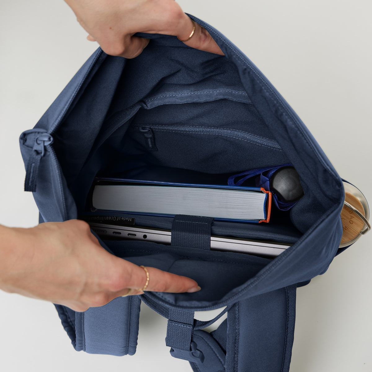ROLLTOP EASY SMALL Rucksack in deep ocean (dunkles Marineblau), Innenansicht mit Laptop und Buch, von Händen geöffnet.