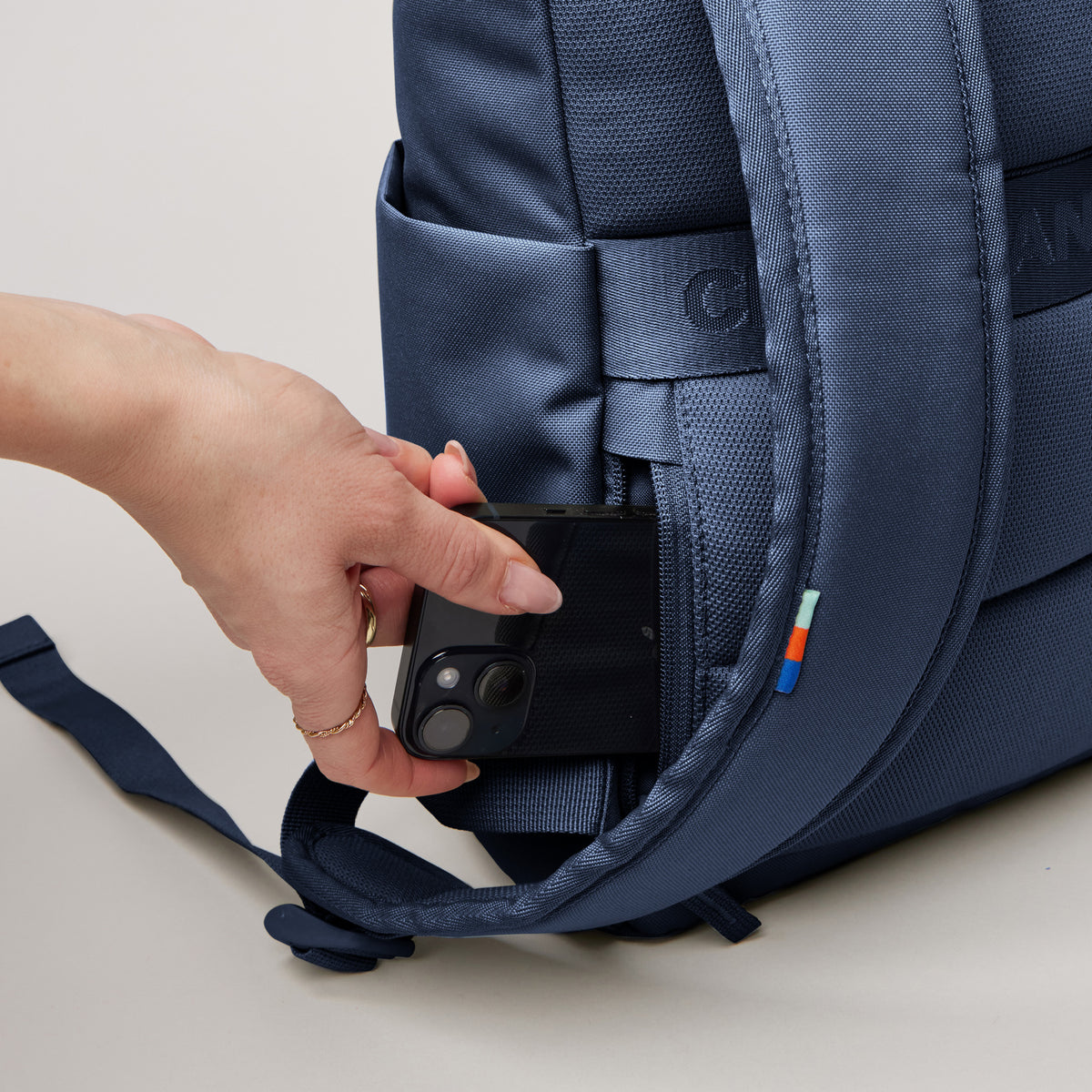 ROLLTOP EASY SMALL Rucksack in deep ocean (dunkles Marineblau), eine Frau steckt ein Smartphone in eine Seitentasche.