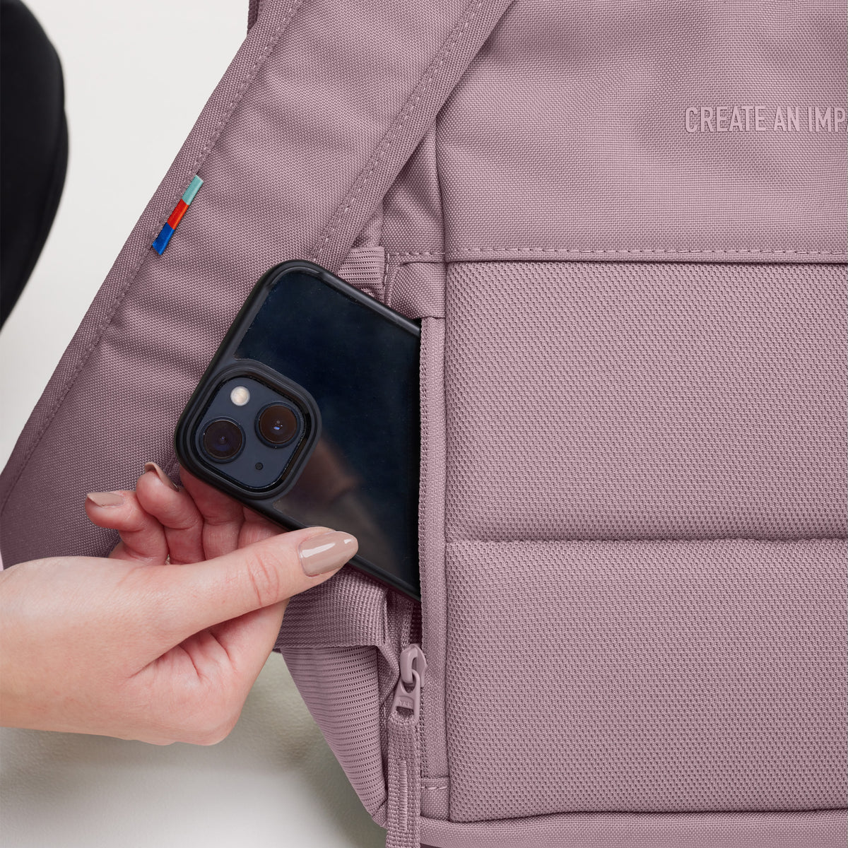 DAYPACK 2.0 Rucksack in calamary (Altrosa), Detailaufnahme einer Frau, die ein Smartphone in eine geheime Tasche steckt.