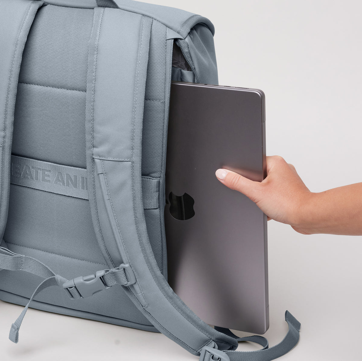 SERENE PACK Rucksack in marlin (grau-blau), eine Hand schiebt einen Laptop in die seitliche Laptoptasche.