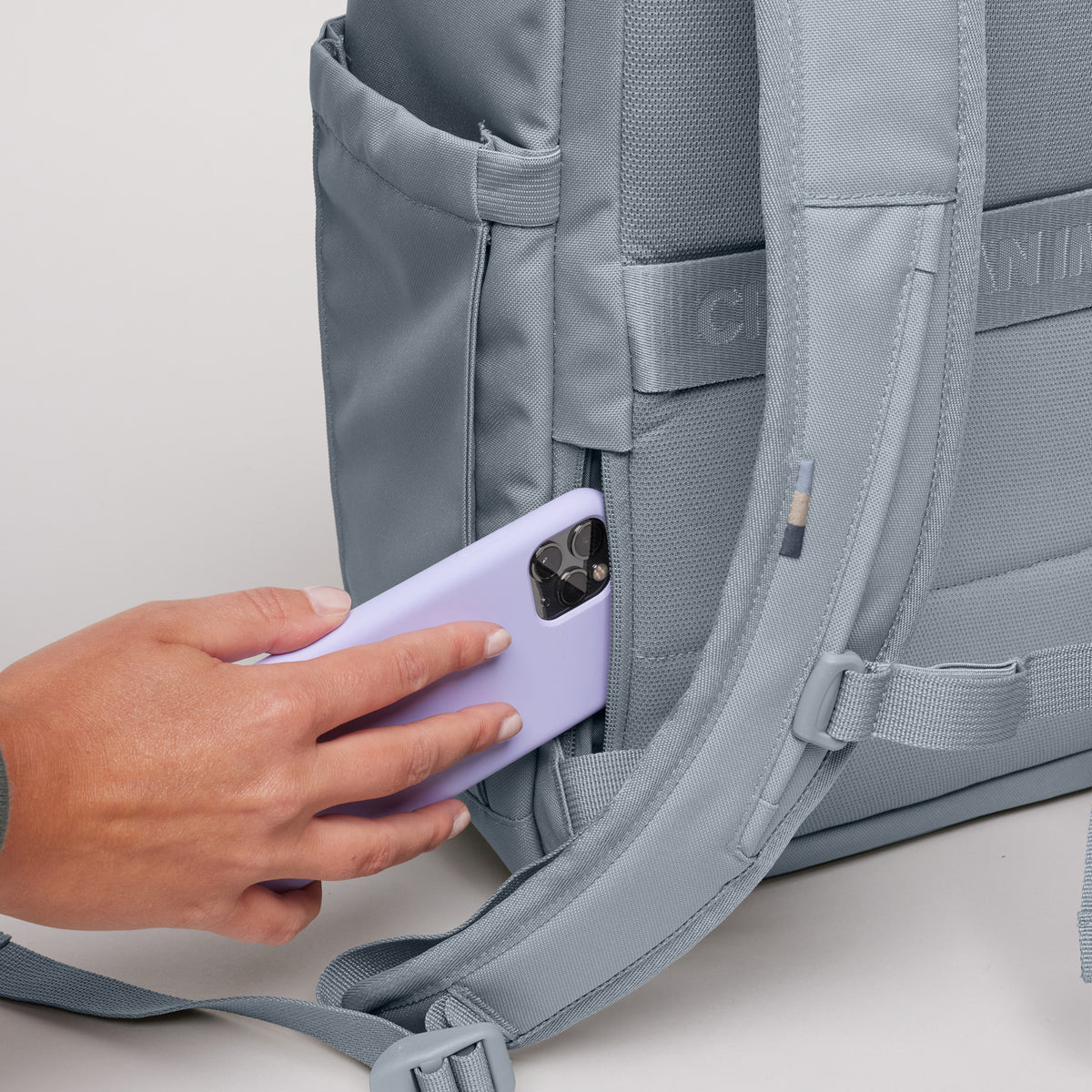 SERENE PACK Rucksack in marlin (grau-blau), Frau steckt Telefon in Seitentasche.