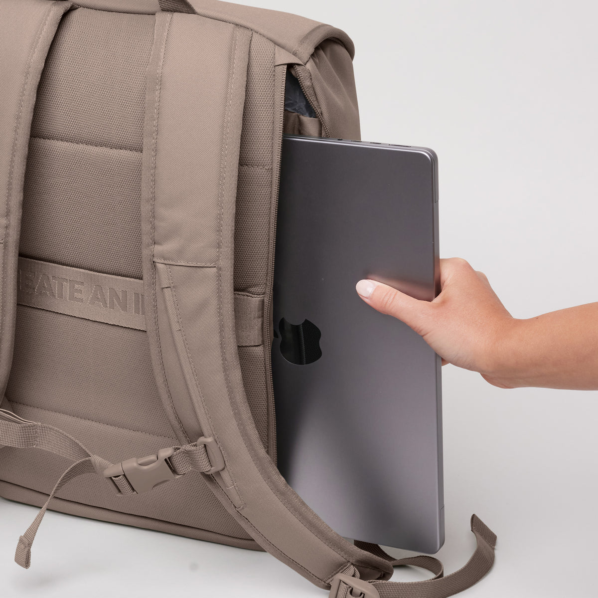 SERENE PACK Rucksack in oyster (klassisches Taupe-Braun), eine Frau steckt einen Laptop hinein.