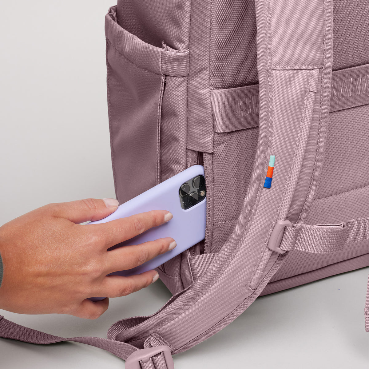 SERENE PACK Rucksack in calamary (Altrosa), eine Hand steckt Smartphone in die Geheimtasche.