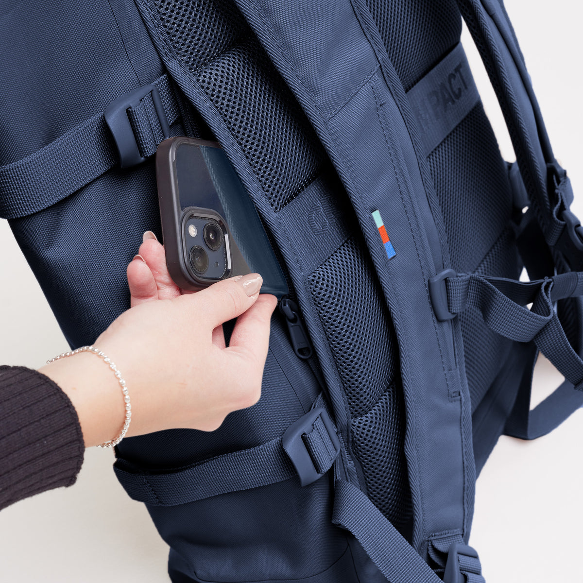 ROLLTOP 2.0 Rucksack in deep ocean (dunkles Marineblau), Detailaufnahme einer Frau, die in die Geheimtasche greift.