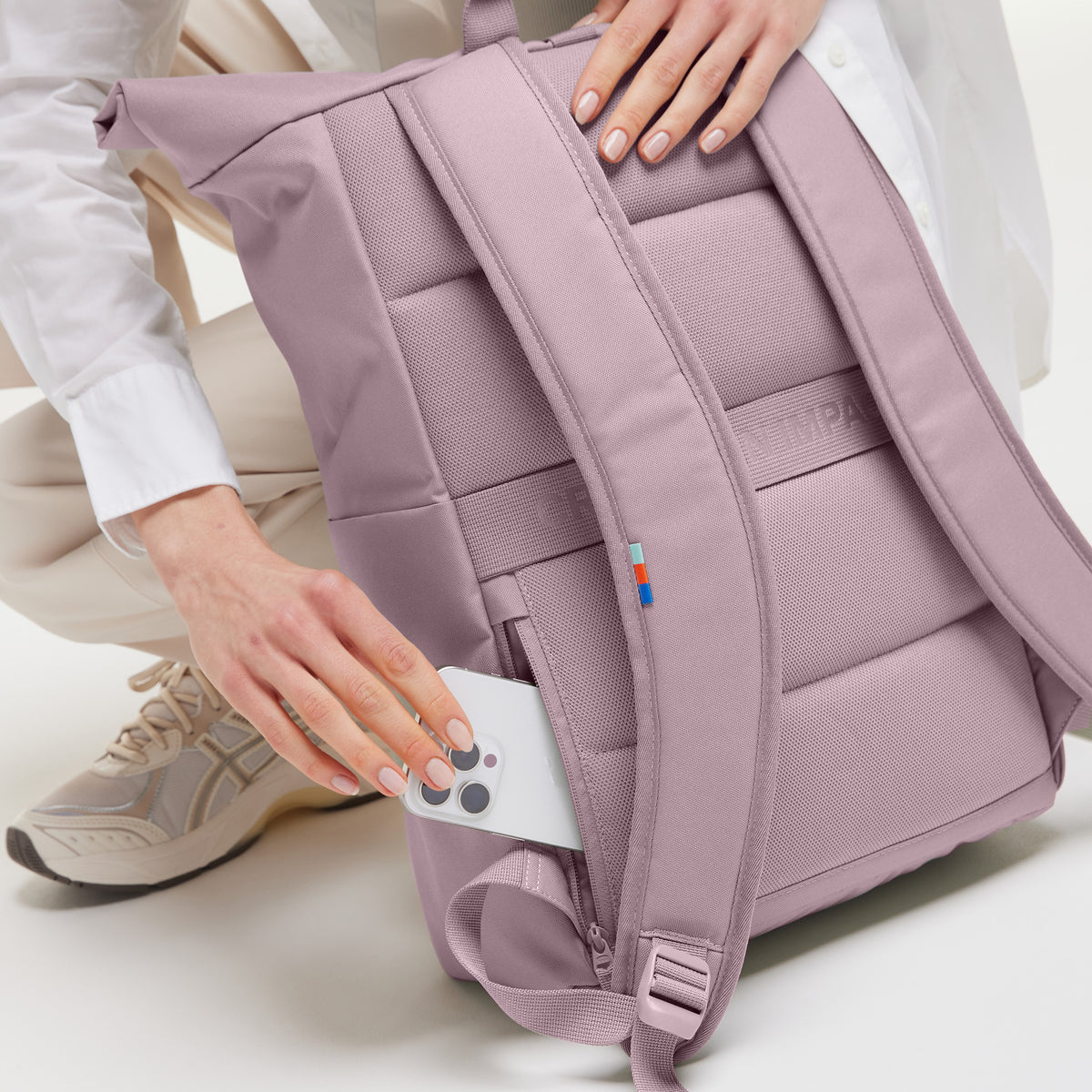 ROLLTOP EASY Rucksack in calamary (Altrosa), eine Frau steckt Handy in die Geheimtasche.