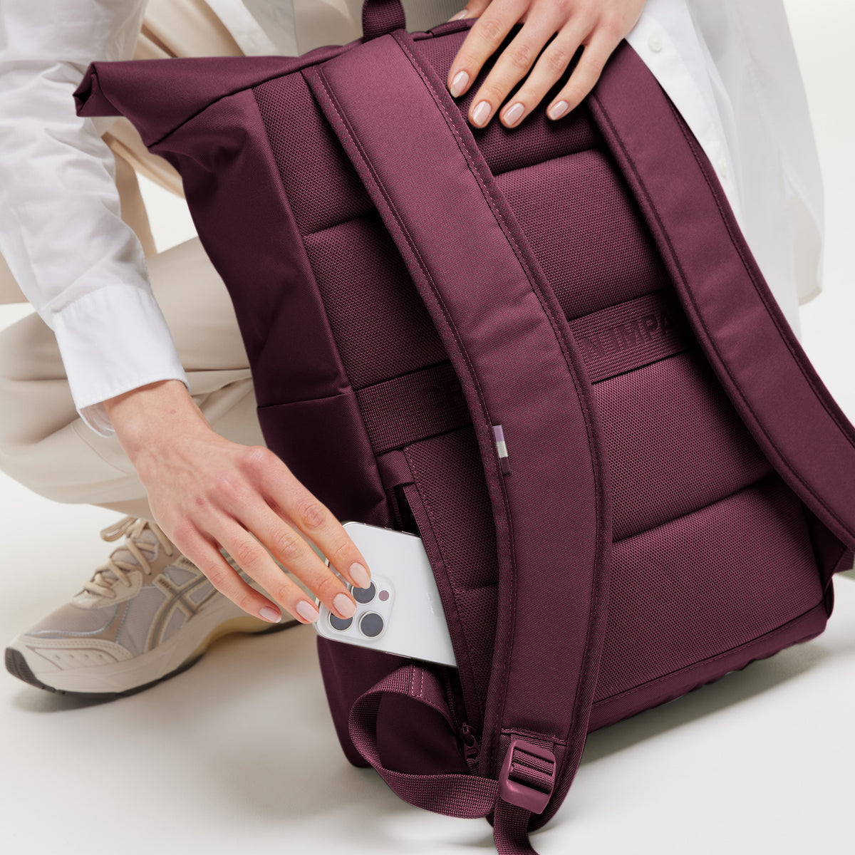 ROLLTOP EASY Rucksack in kraken (Weinrot): Frau steckt Smartphone in Geheimtasche an der Seite.