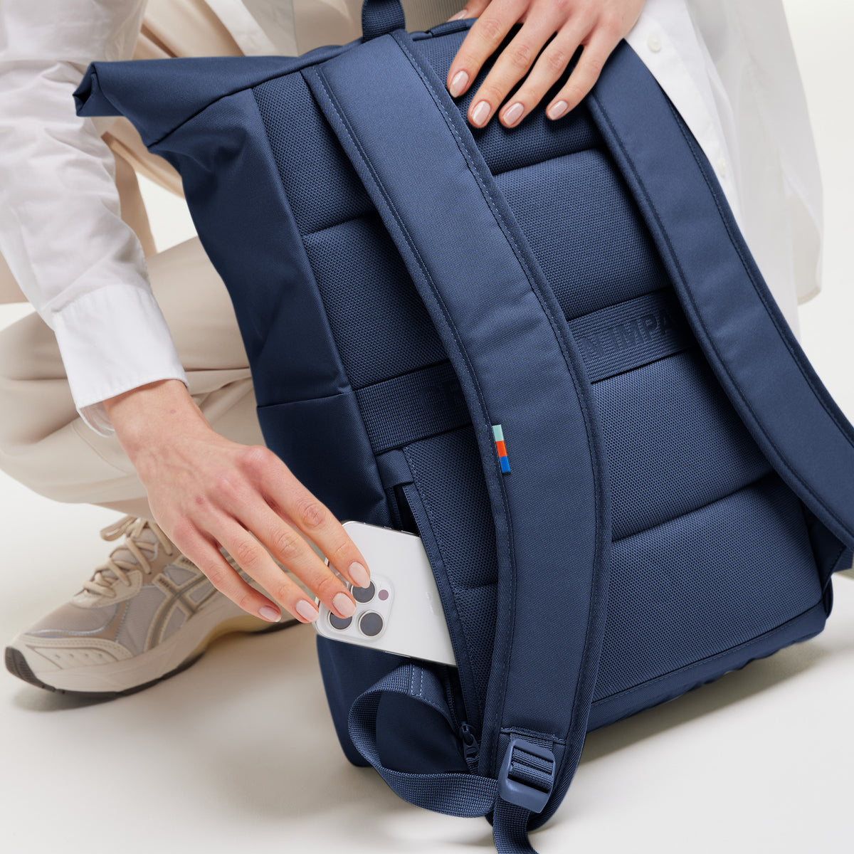 ROLLTOP EASY Rucksack in deep ocean (dunkles Marineblau). Eine Frau steckt ein Smartphone in eine geheime Tasche.