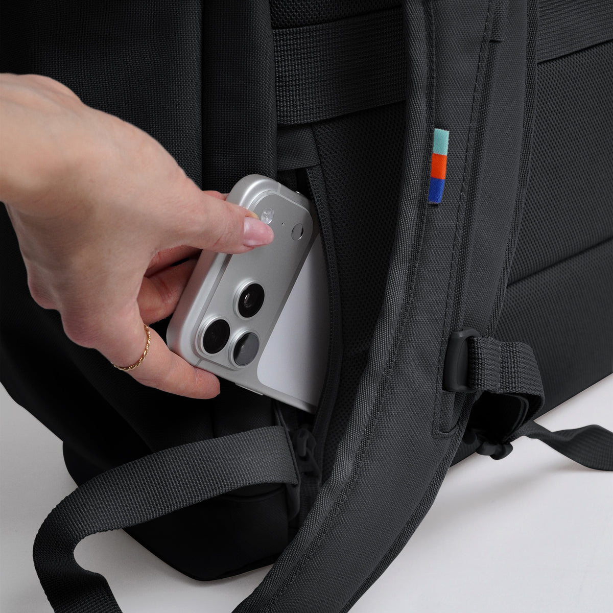 FLAP PACK LARGE Rucksack in black (Schwarz) von einer Frau ein Smartphone in die Geheimtasche gesteckt.