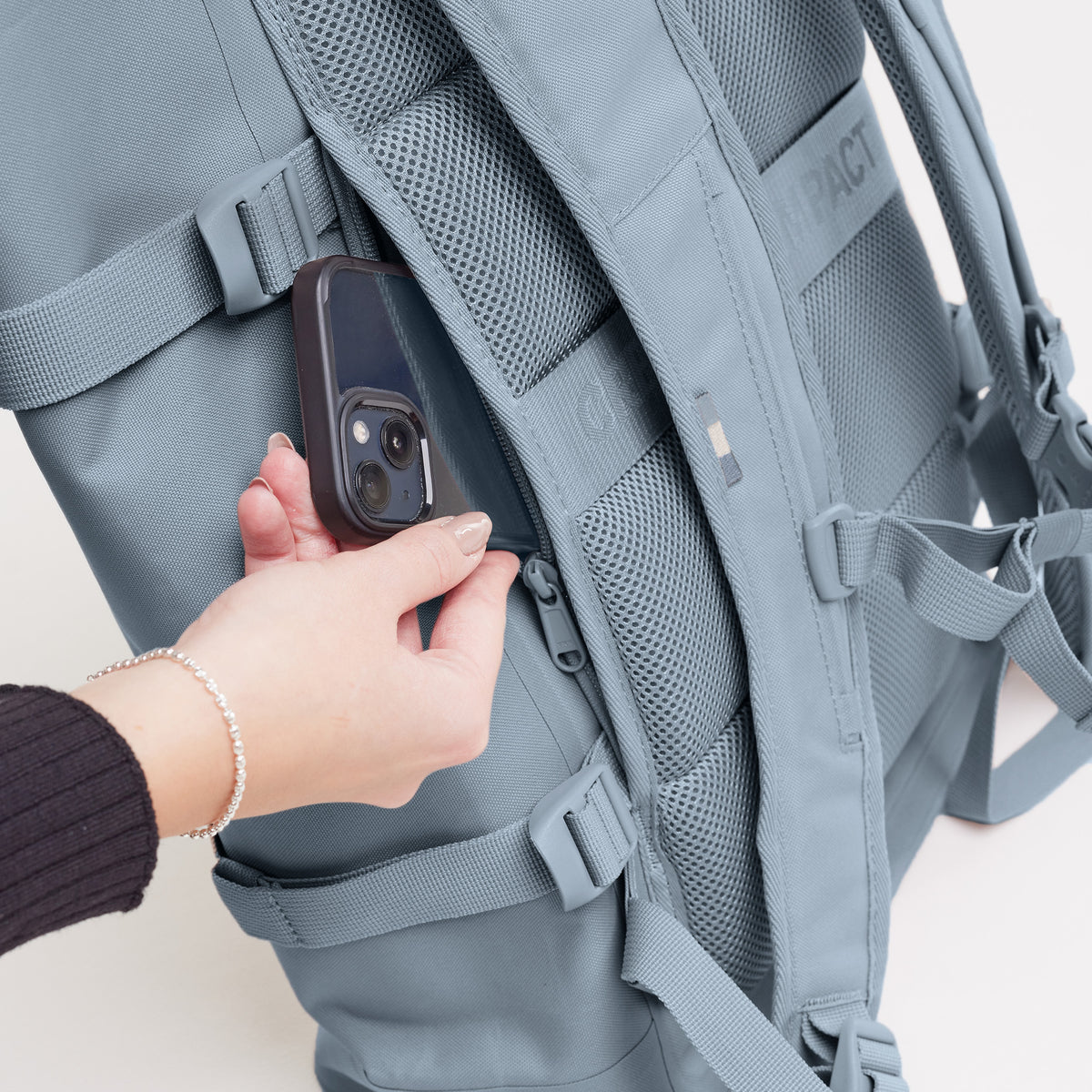 ROLLTOP 2.0 MONOCHROME EDITION Rucksack in marlin (grau-blau), eine Frau steckt Smartphone in Geheimtasche.