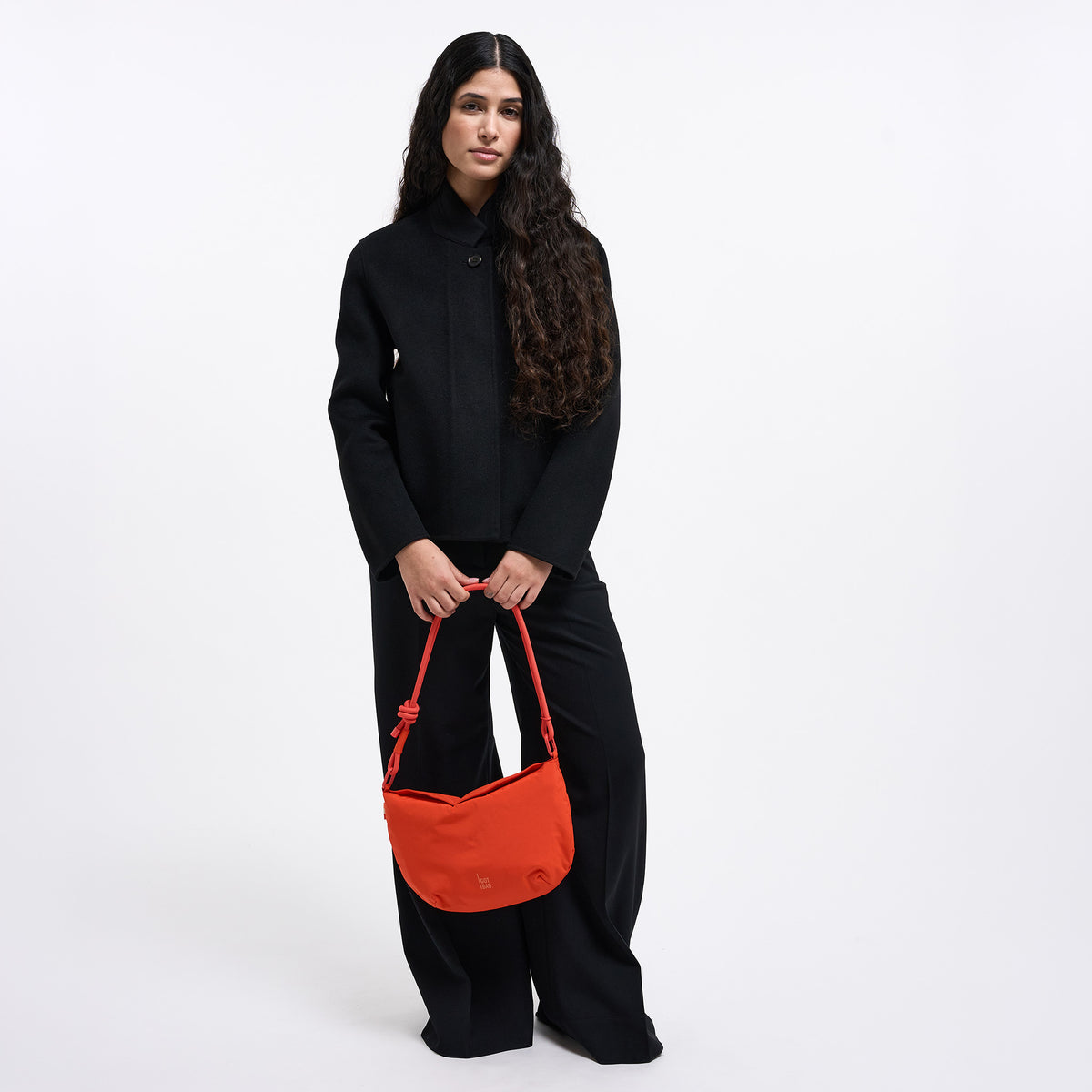 CLAM BAG Tasche in hot coral (knalliges Orange) von einer Frau in der Hand gehalten.