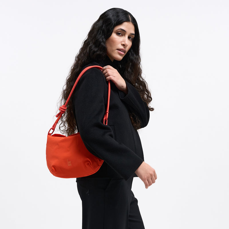 CLAM BAG Tasche in hot coral (knalliges Orange) von einer Frau über der Schulter getragen.