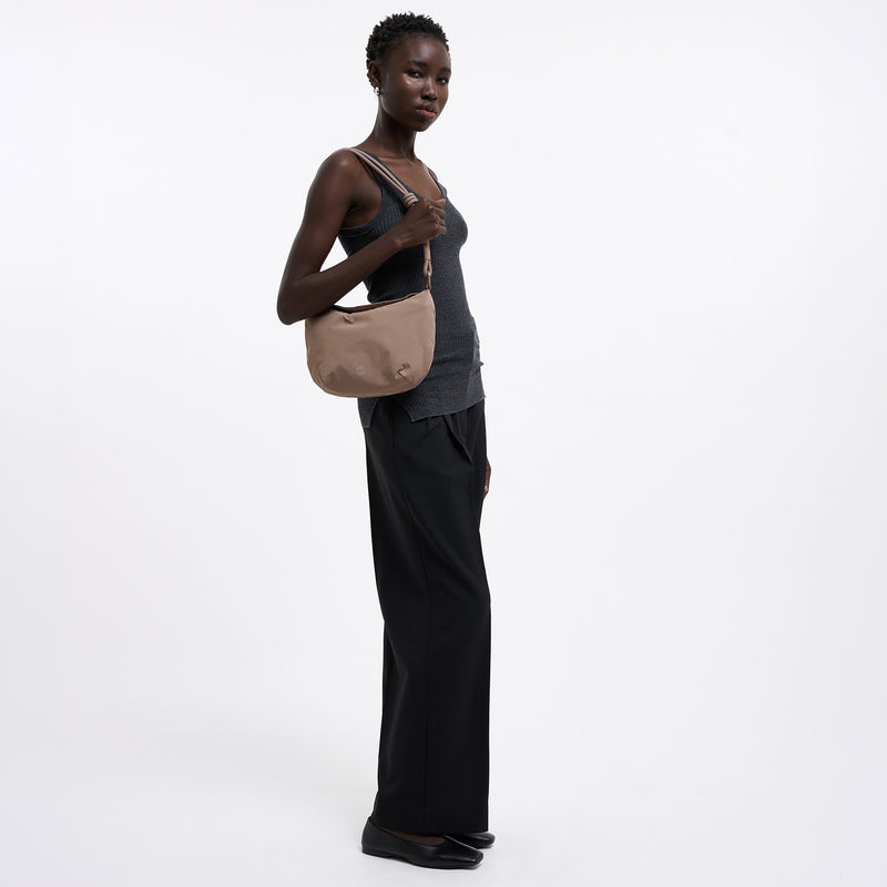 CLAM BAG Tasche in oyster (klassisches Taupe-Braun) von einer Frau über der Schulter getragen.