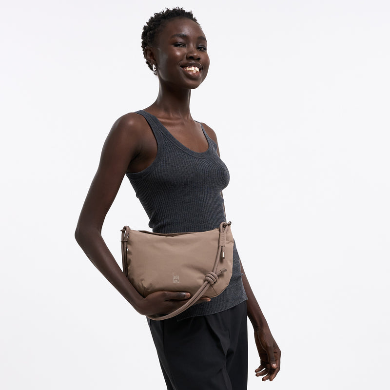 CLAM BAG Tasche in oyster (klassisches Taupe-Braun) von einer Frau in der Hand gehalten.