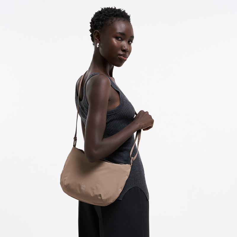 CLAM BAG Tasche in oyster (klassisches Taupe-Braun) von einer Frau über der Schulter getragen.