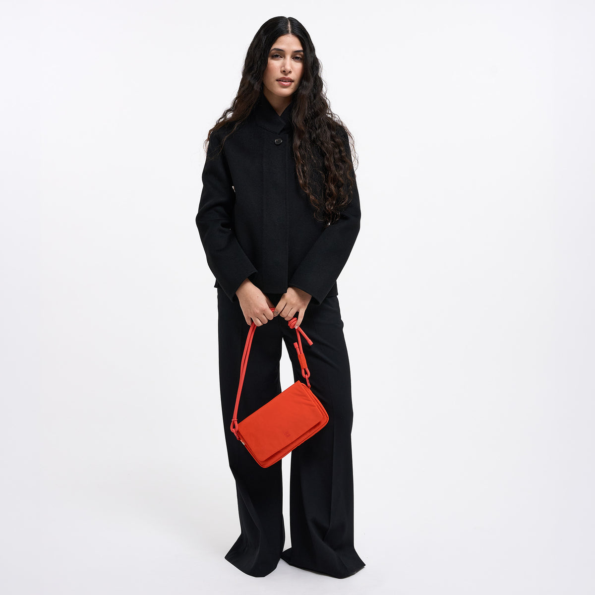 FACET BAG Tasche in hot coral (knalliges Orange) von einer Frau in der Hand gehalten.