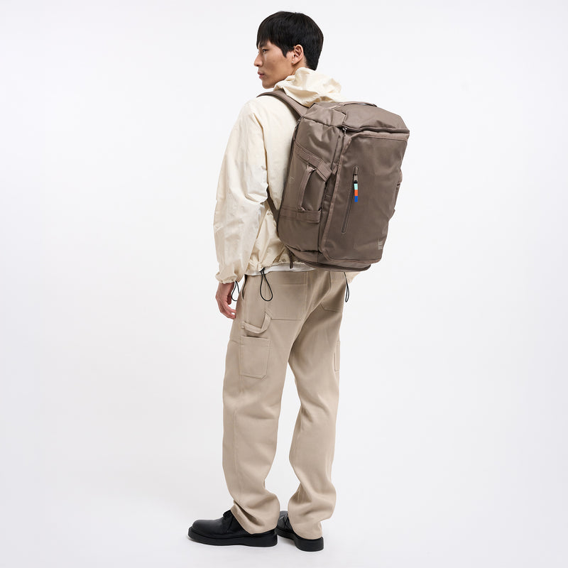 DUFFLE PACK Rucksack in oyster (klassisches Taupe-Braun) von einem Mann auf dem Rücken getragen.