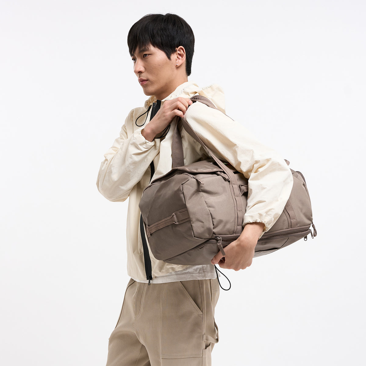 DUFFLE PACK Tasche in oyster (klassisches Taupe-Braun) von einem Mann über der Schulter getragen.