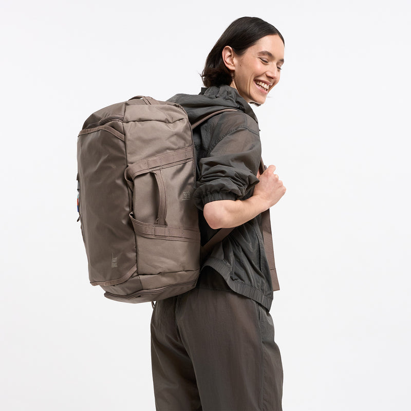 DUFFLE PACK Rucksack in oyster (klassisches Taupe-Braun) von einer Frau als Rucksack auf dem Rücken getragen.