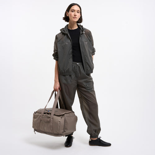 DUFFLE PACK Tasche in oyster (klassisches Taupe-Braun) von einer Frau in der Hand gehalten.
