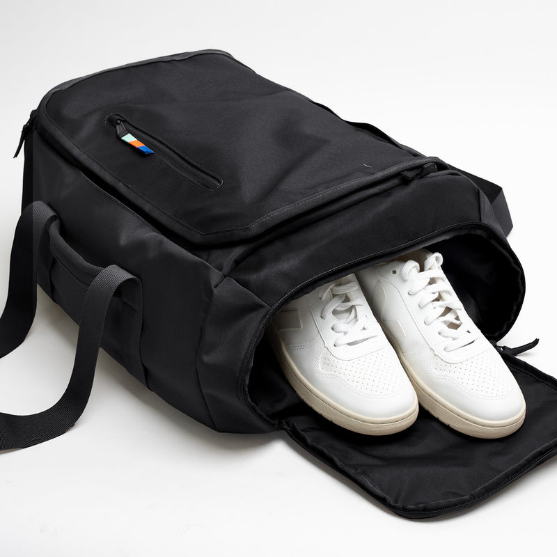 DUFFLE PACK Tasche in black (Schwarz) mit weißen Sneakern in einem offenen Seitenfach.