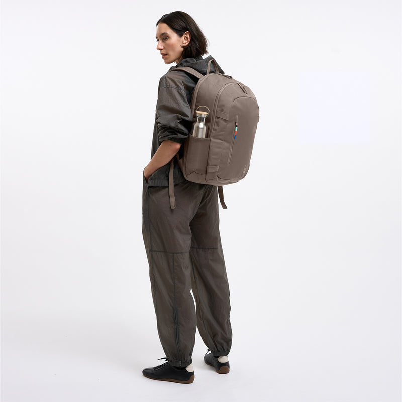 HYBRID PACK Rucksack in oyster (klassisches Taupe-Braun) von einer Frau auf dem Rücken getragen, mit Wasserflasche.