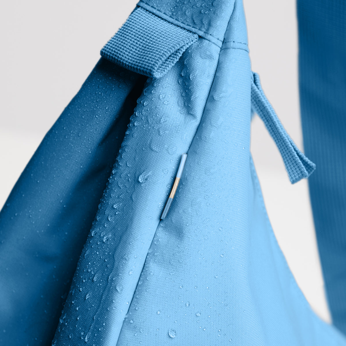MOON BAG LARGE Tasche in aqua (leuchtendes Hellblau) als Detailaufnahme mit Wassertropfen auf dem Stoff.