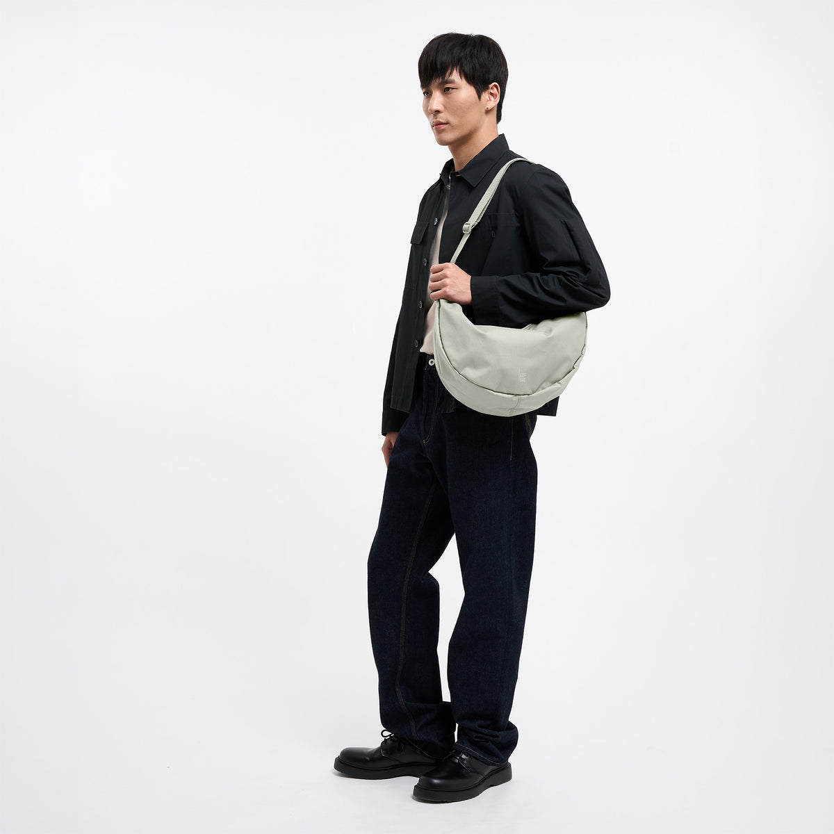 MOON BAG LARGE Tasche in beach foam (helles Grau) von einem Mann über der Schulter getragen.