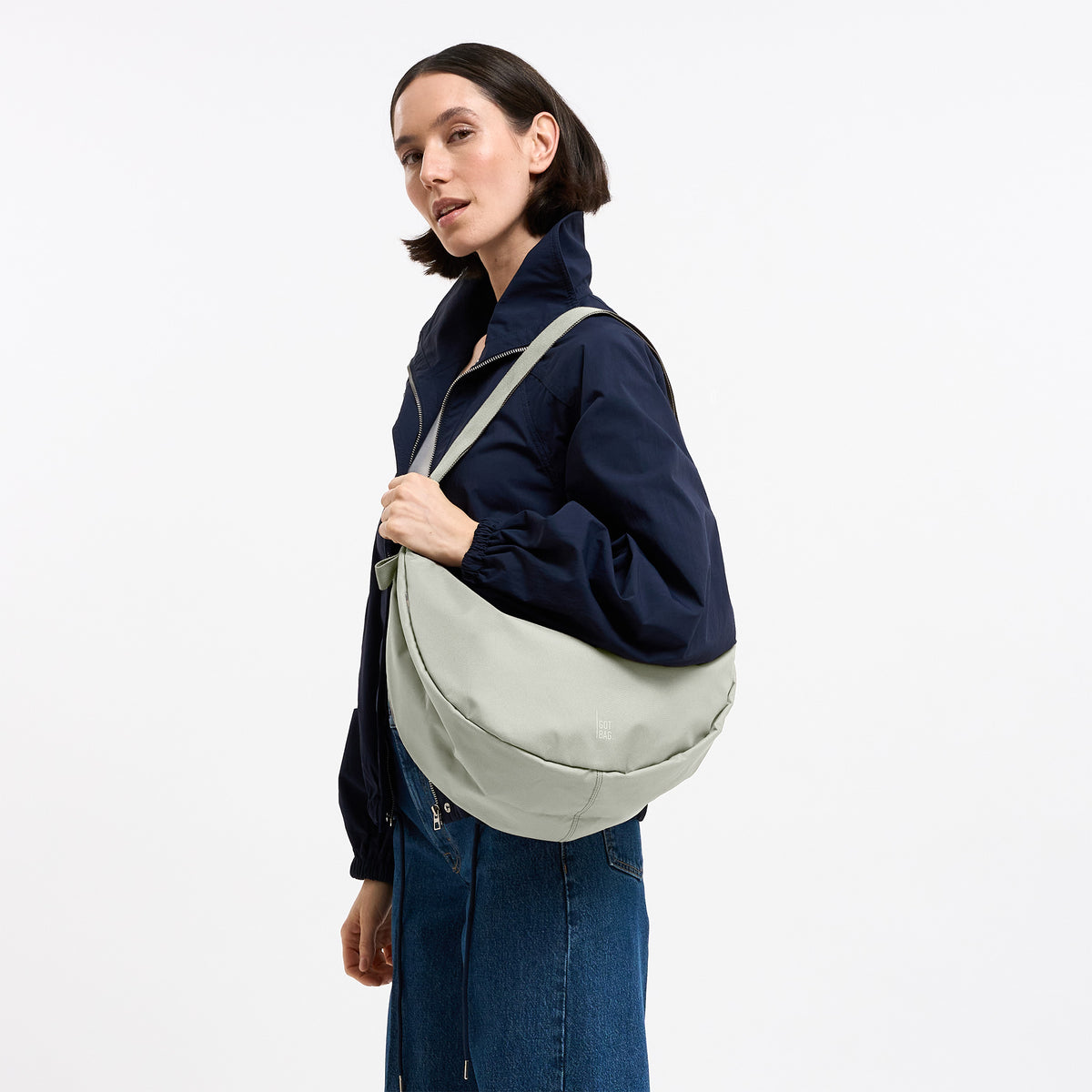 MOON BAG LARGE Tasche in beach foam (helles Grau) von einer Frau über der Schulter getragen.