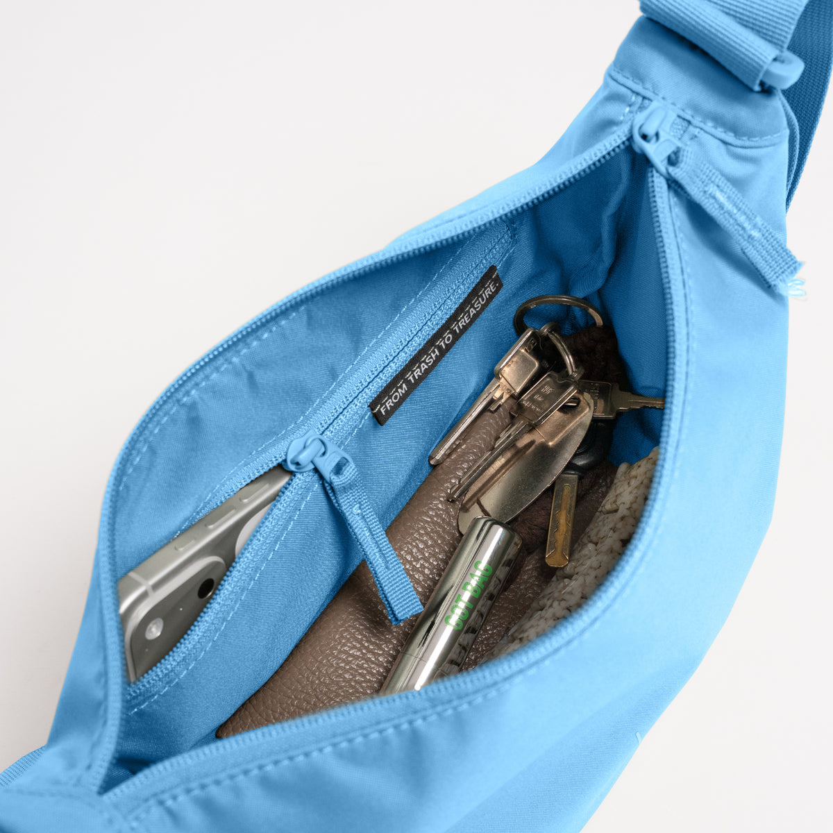 MOON BAG SMALL Monochrome Edition Tasche in aqua (leuchtendes Hellblau) Detailaufnahme des Innenraums mit Handy und Schlüsseln.