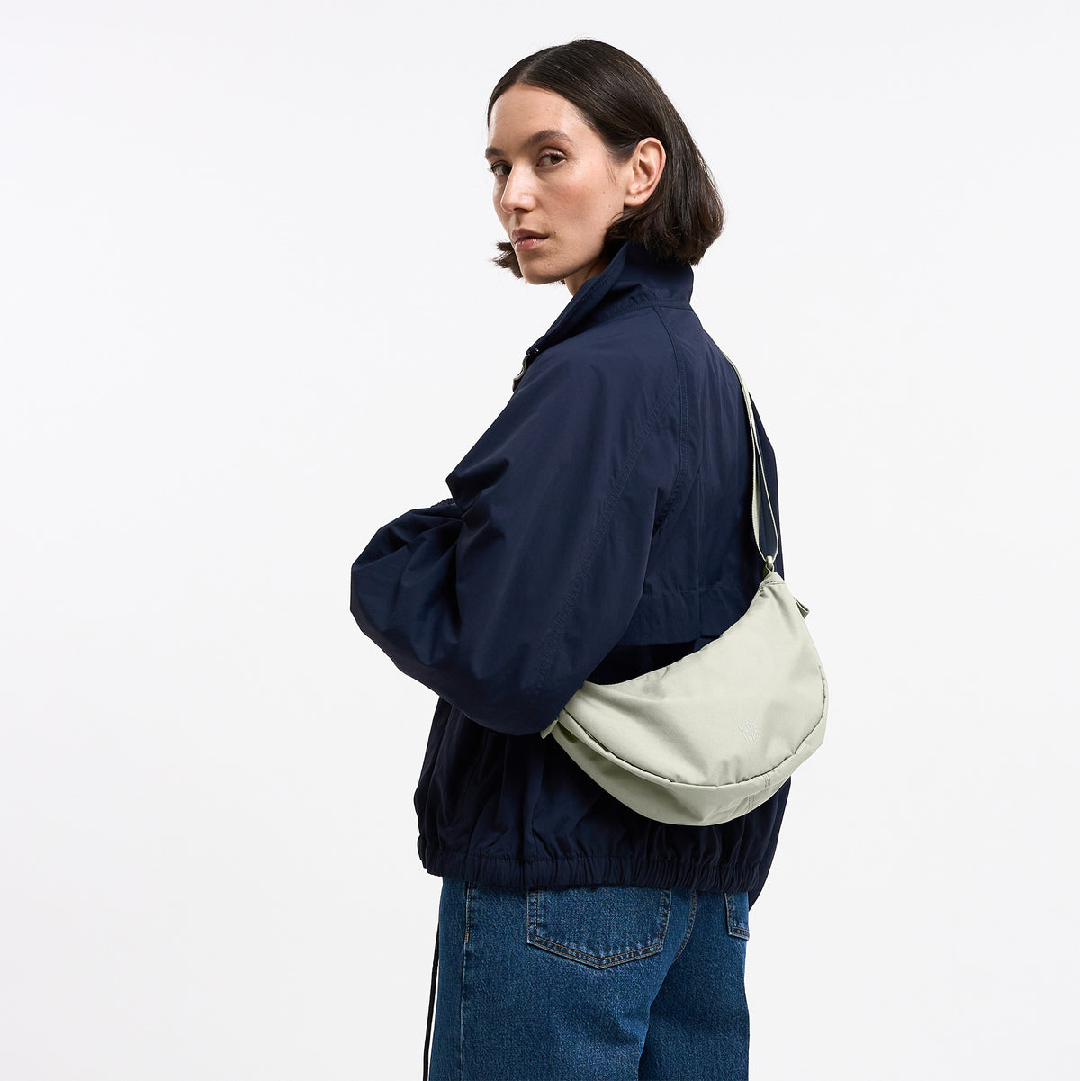 MOON BAG SMALL Tasche in beach foam (helles Grau) von einer Frau crossbody getragen.