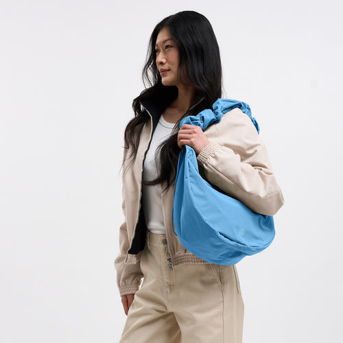 MOON BAG RUFFLE Tasche in aqua (leuchtendes Hellblau) von einer Frau über der Schulter getragen.