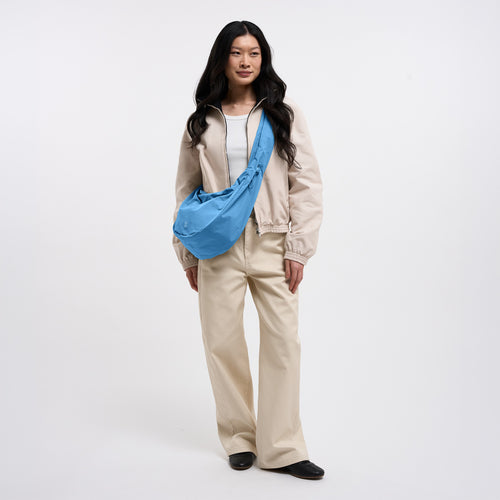 MOON BAG RUFFLE Tasche in aqua (leuchtendes Hellblau) von einer Frau crossbody getragen.