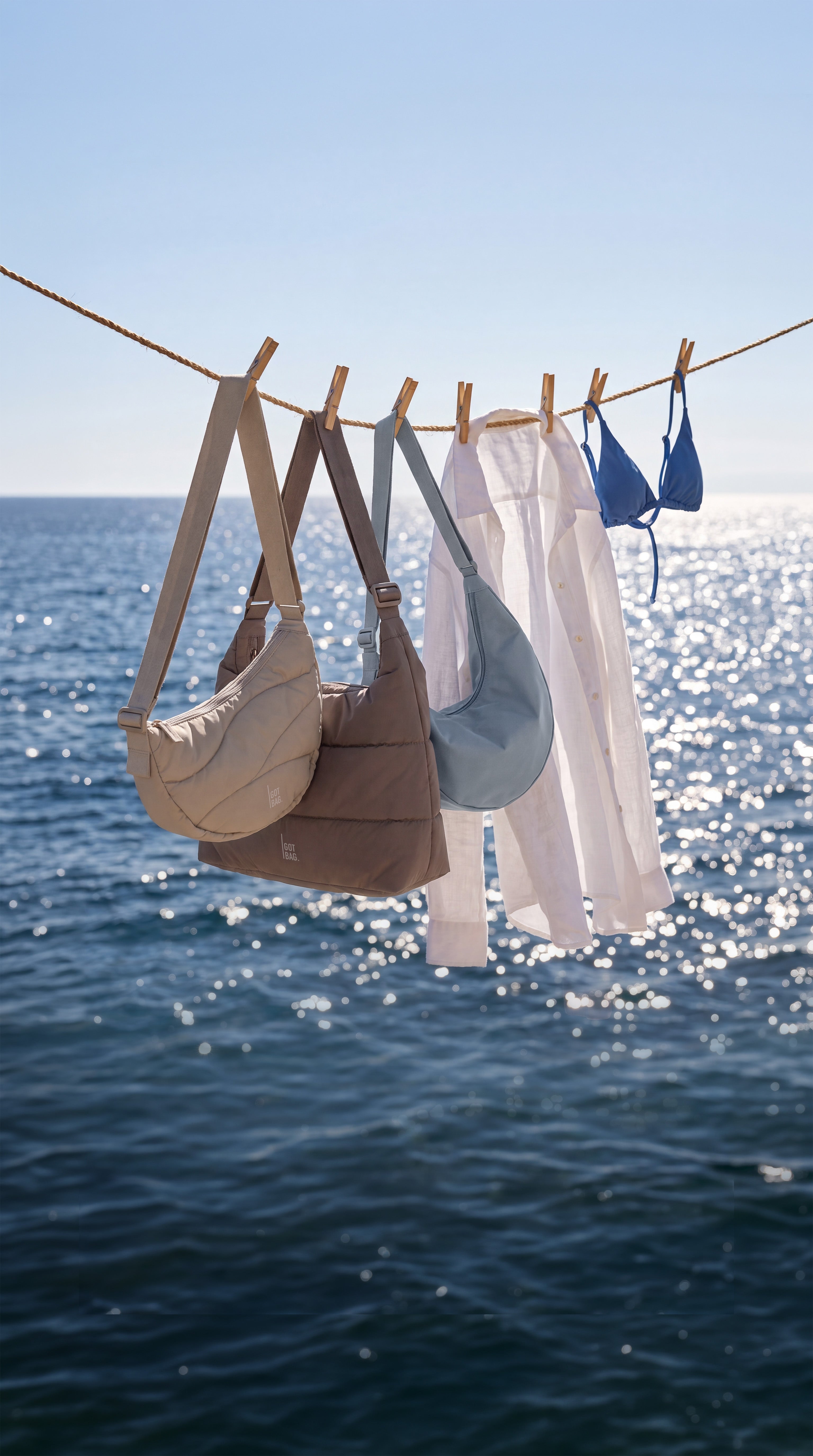 Three bags, a shirt, and a bikini top hang on a clothesline above the sea.