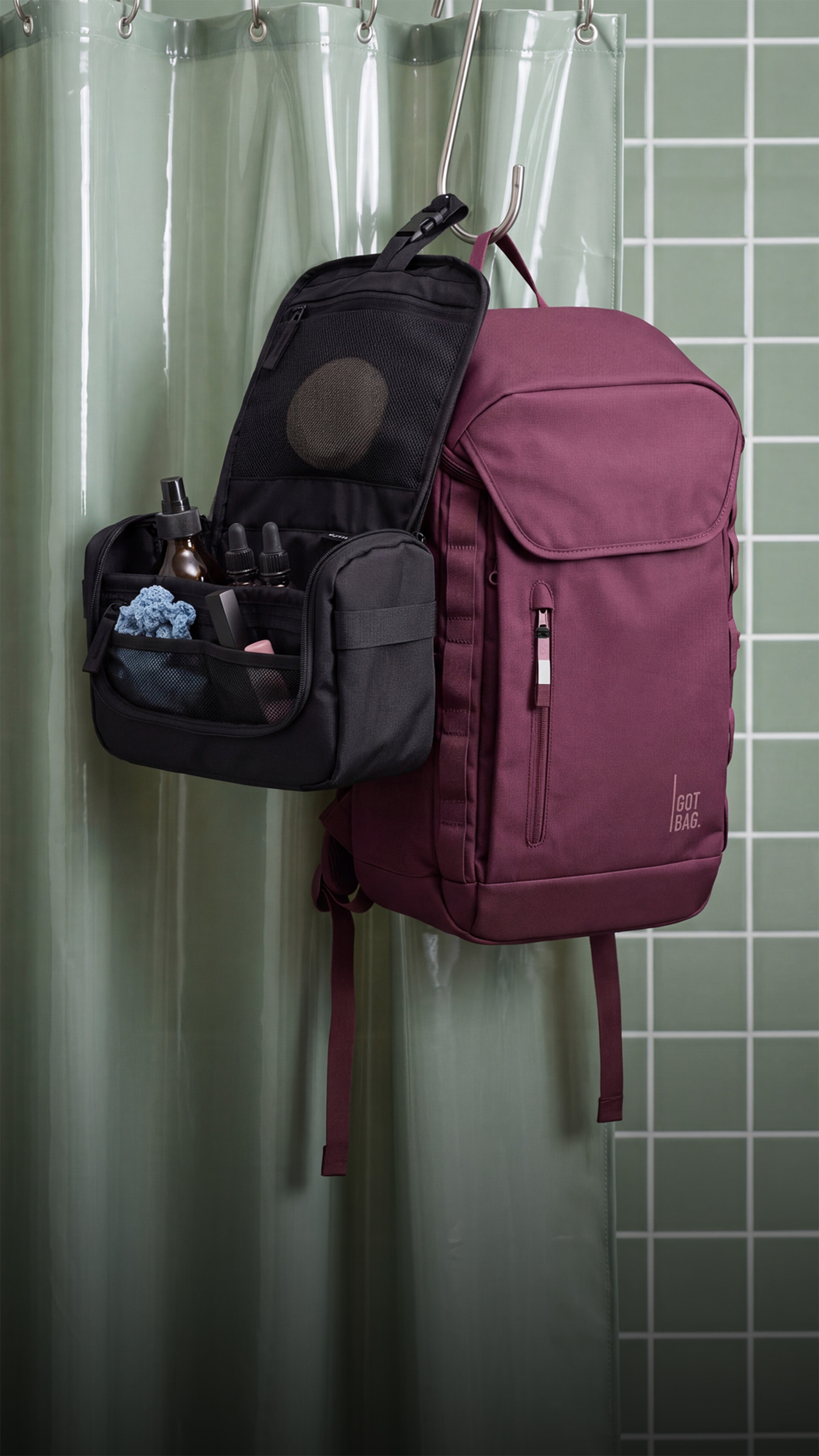 FREE SHOWER KIT accessories with open compartments and care products, hanging next to a backpack on a shower curtain rod.