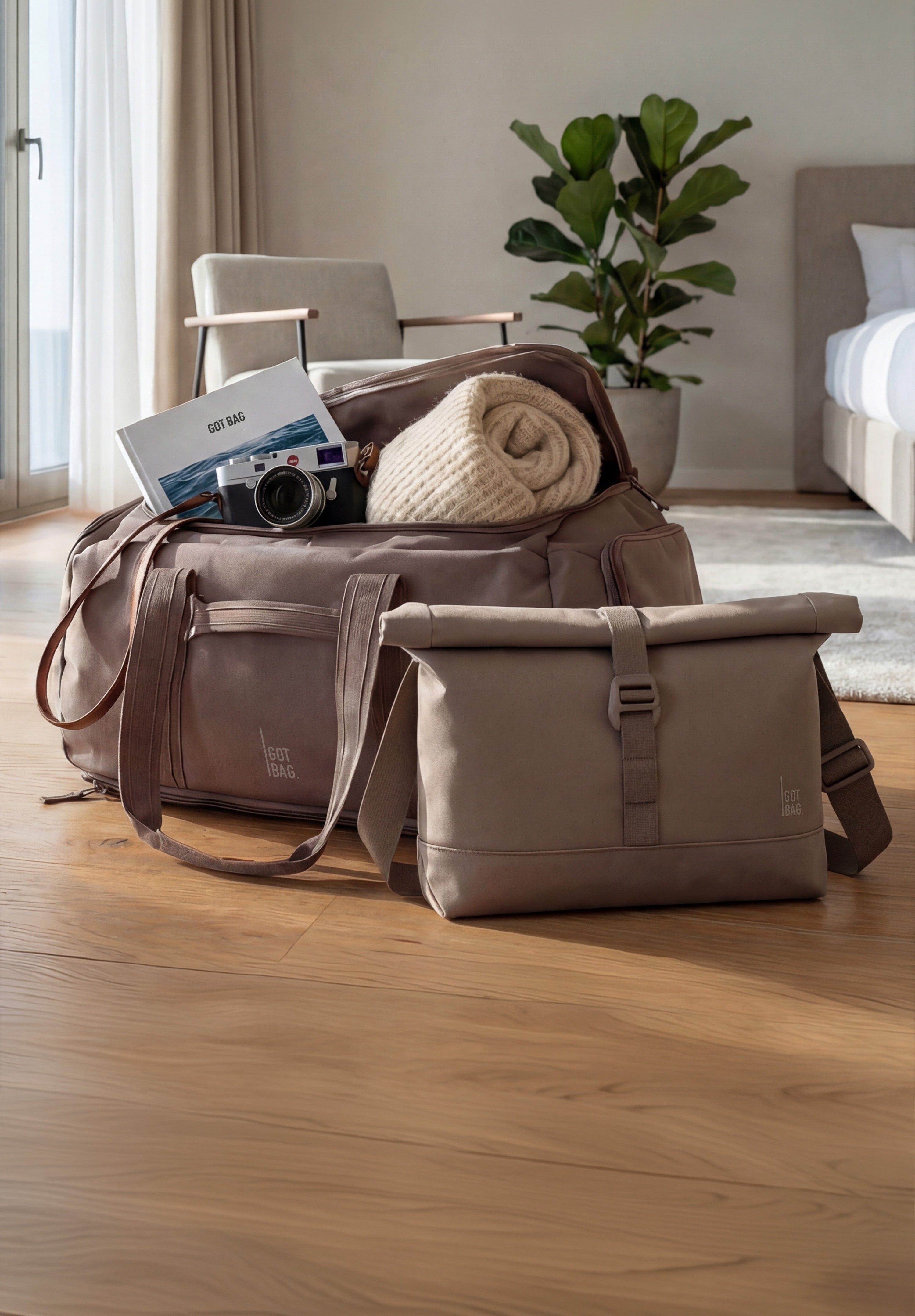 Dvě tašky na dřevěné podlaze. Velká cestovní taška otevřená s knihou, dekou, fotoaparátem. Taška přes rameno vedle.