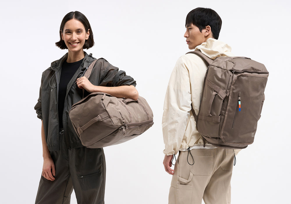 Žena s krátkými vlasy se usmívá a ležérně nese prostornou tašku v ruce, která jí spočívá na boku.