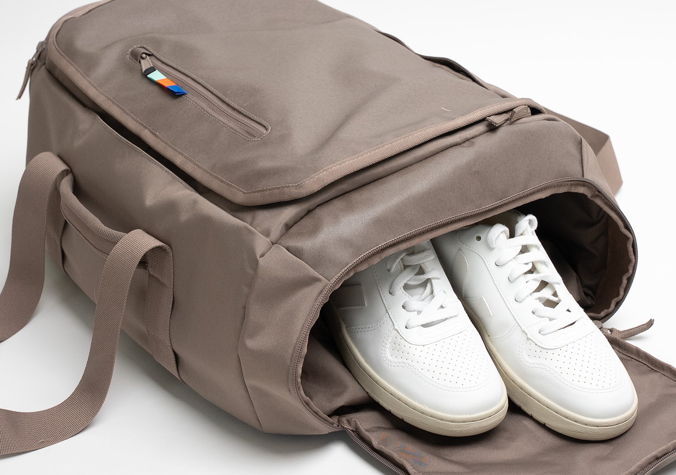 Taška s otevřenou boční přihrádkou, uvnitř bílé tenisky. Horní kapsa s barevným zipem.