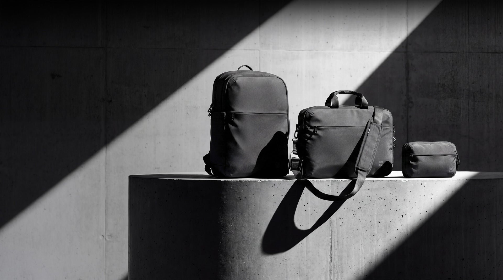 Accessoires: Rucksack, Umhängetasche und kleiner Beutel auf Beton mit Licht und Schatten.