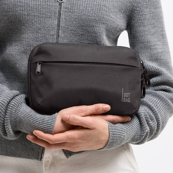 COMMUTER TECH POUCH Accessoire in black (Schwarz) von einer Frau in den Händen gehalten.